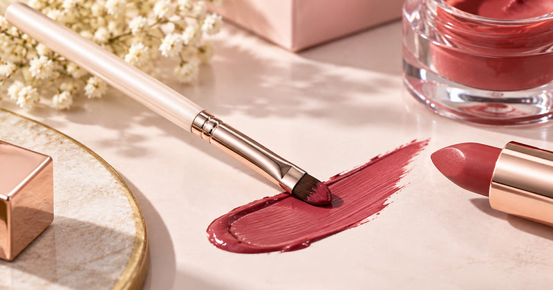 Makeup artist using a small lip brush to apply red lipstick with a crisp edge