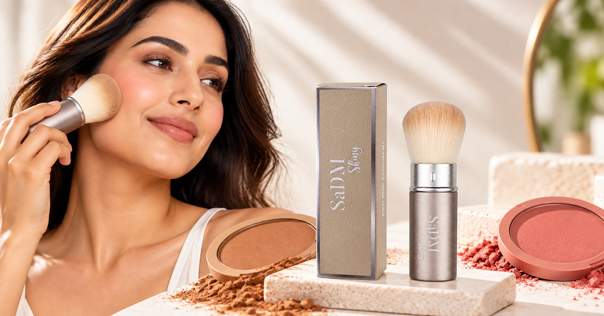Hand holding a kabuki brush above bronzer and blush powders on a vanity