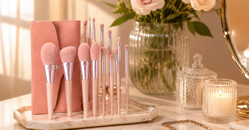 Pink makeup brush set with a coral pouch standing on a vanity tray beside a perfume bottle and candle